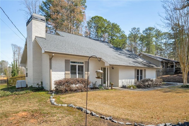 view of front of house with fence, roof with shingles, a chimney, a front lawn, and brick siding