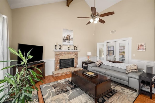 living area with visible vents, wood finished floors, a wainscoted wall, and vaulted ceiling with beams