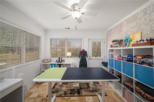 recreation room featuring visible vents, brick wall, crown molding, and a ceiling fan