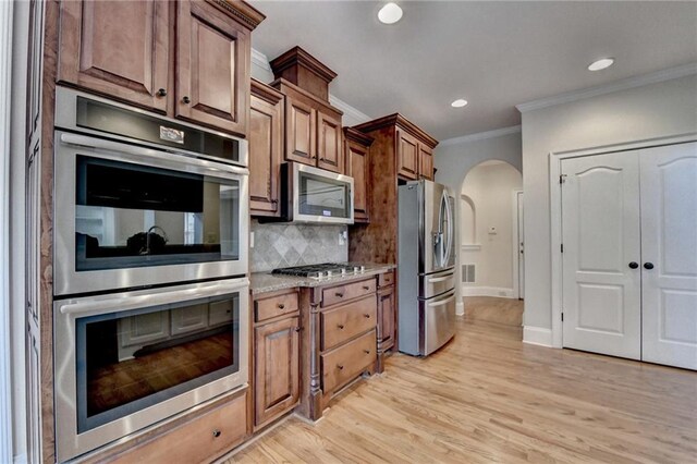 1054 Morgan Garner Dr SW, Lilburn, GA 30047 - kitchen featuring appliances with stainless steel finishes, ornamental molding, arched walkways, tasteful backsplash, and light wood-style floors