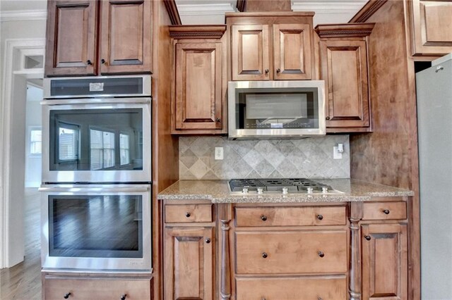 1054 Morgan Garner Dr SW, Lilburn, GA 30047 - kitchen featuring appliances with stainless steel finishes, ornamental molding, decorative backsplash, light stone countertops, and brown cabinets