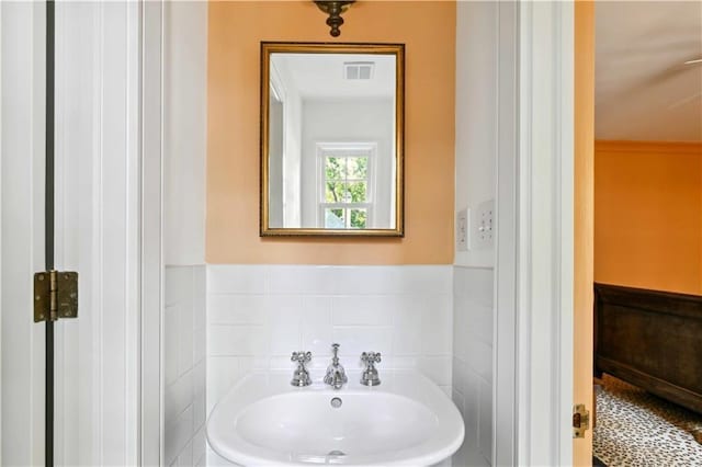 bathroom featuring visible vents, wainscoting, tile walls, and a sink