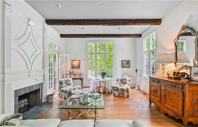 living area featuring a fireplace, beam ceiling, wood finished floors, and baseboards