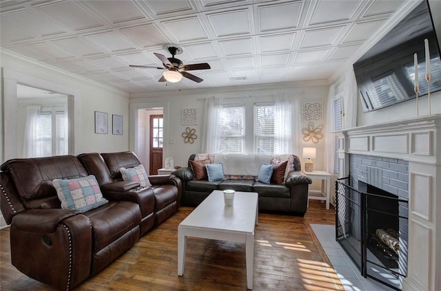 living area with an ornate ceiling, a fireplace, wood-type flooring, ornamental molding, and a ceiling fan