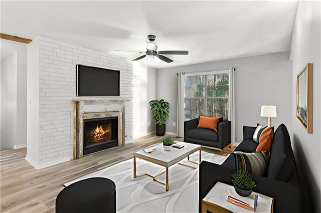 living room with a fireplace, ceiling fan, and light wood-type flooring