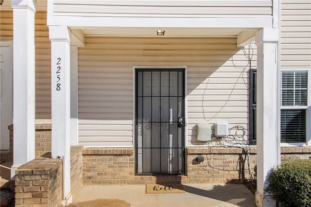 view of exterior entry featuring covered porch and brick siding