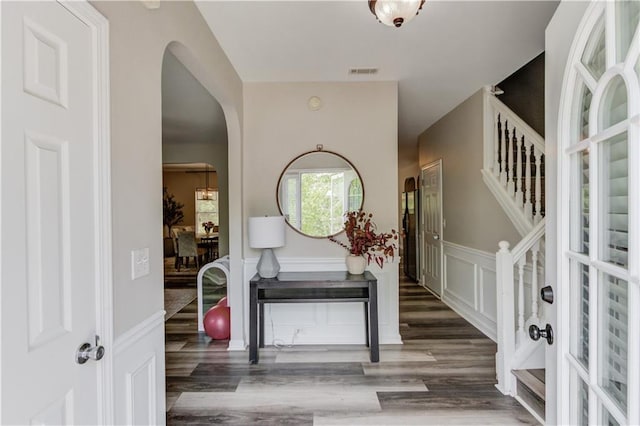 entryway with arched walkways, a wainscoted wall, wood finished floors, visible vents, and stairs