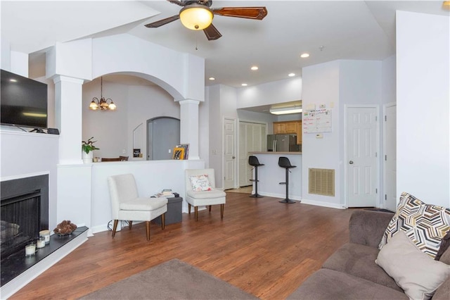 living room with wood-type flooring, ceiling fan with notable chandelier, and decorative columns