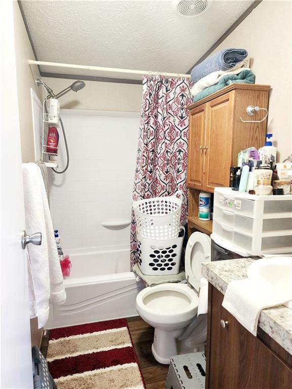 full bathroom featuring toilet, a textured ceiling, vanity, shower / bath combo, and hardwood / wood-style flooring