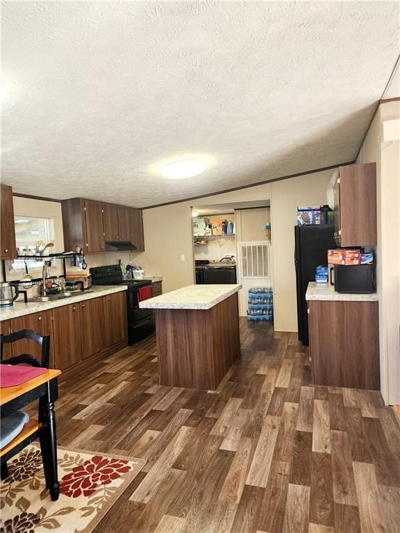 kitchen with separate washer and dryer, a center island, black appliances, dark wood-type flooring, and a textured ceiling