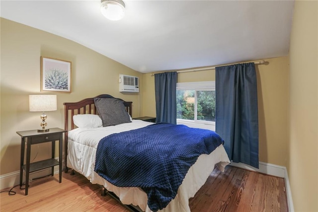 bedroom with lofted ceiling, a wall mounted air conditioner, and wood-type flooring