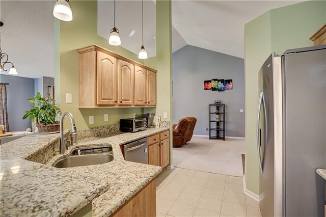 kitchen featuring light stone counters, vaulted ceiling, stainless steel appliances, light brown cabinets, and a sink