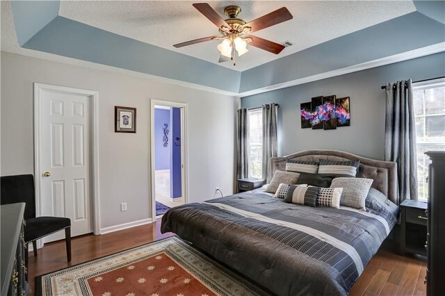 bedroom featuring a tray ceiling, visible vents, baseboards, and wood finished floors