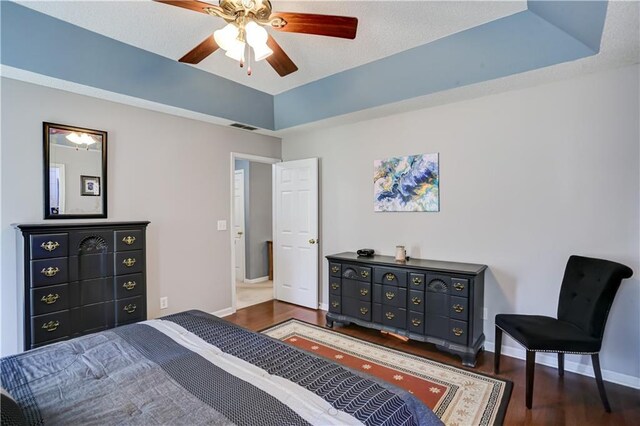 bedroom with a tray ceiling, visible vents, a ceiling fan, wood finished floors, and baseboards