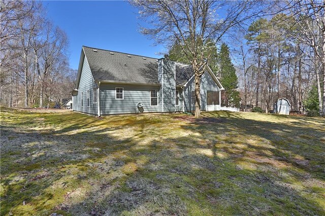 back of property featuring an outbuilding, a storage shed, a lawn, and a shingled roof