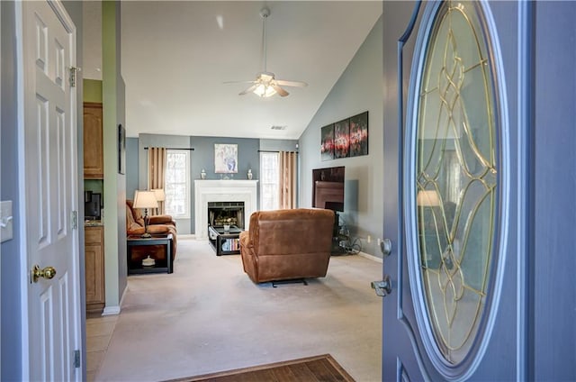 carpeted living area with ceiling fan, a fireplace, visible vents, baseboards, and vaulted ceiling