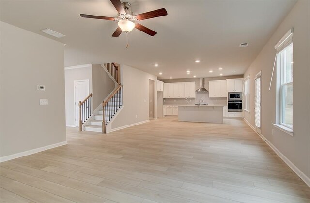 kitchen with appliances with stainless steel finishes, sink, wall chimney range hood, a center island with sink, and white cabinetry