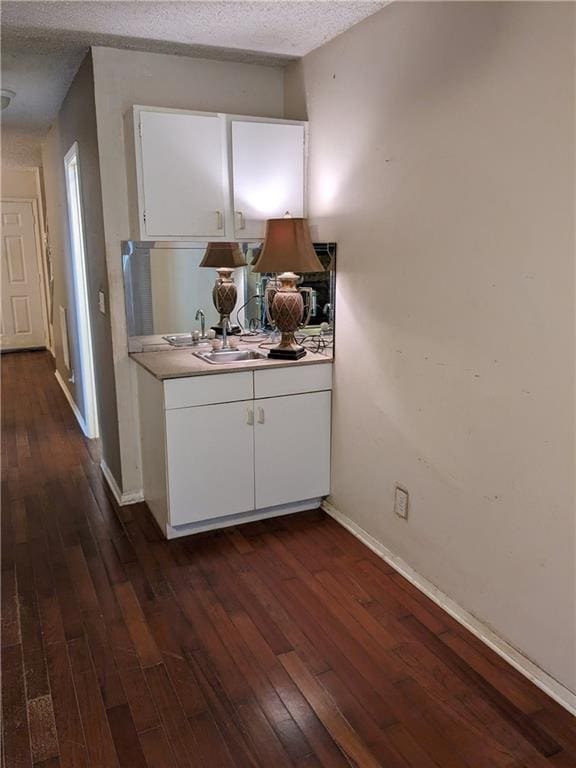 bar featuring dark wood-style flooring, a textured ceiling, baseboards, and a sink