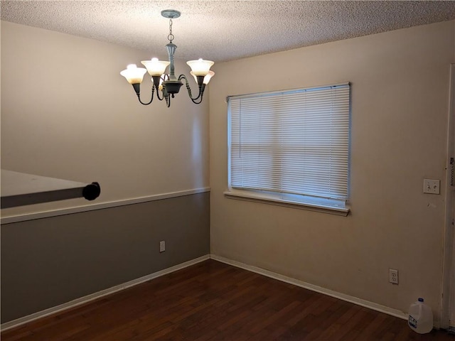 empty room with a notable chandelier, a textured ceiling, baseboards, and wood finished floors