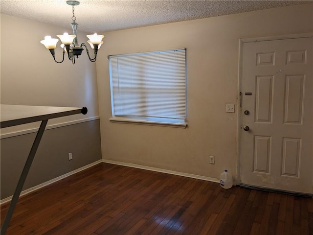 unfurnished dining area with a notable chandelier, baseboards, wood-type flooring, and a textured ceiling