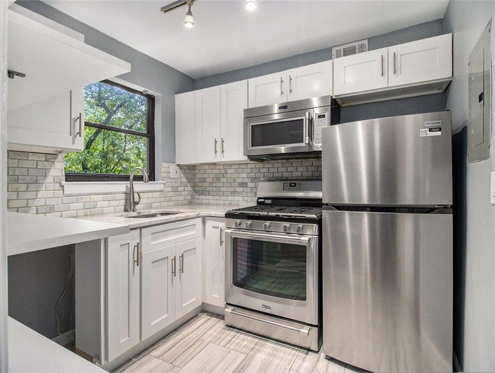 kitchen featuring appliances with stainless steel finishes, backsplash, white cabinetry, and sink