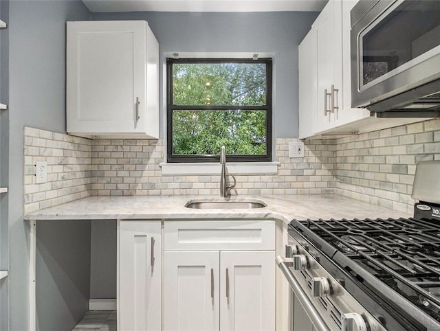 kitchen featuring decorative backsplash, light stone countertops, stainless steel appliances, sink, and white cabinets