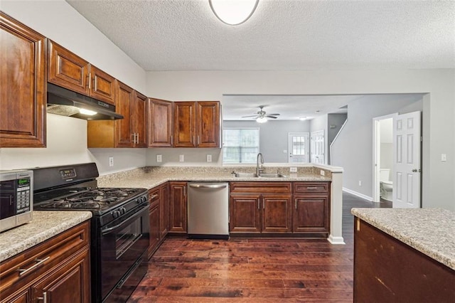 kitchen with appliances with stainless steel finishes, under cabinet range hood, a sink, dark wood finished floors, and a peninsula