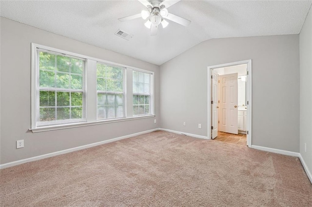empty room with light carpet, a ceiling fan, vaulted ceiling, baseboards, and a textured ceiling