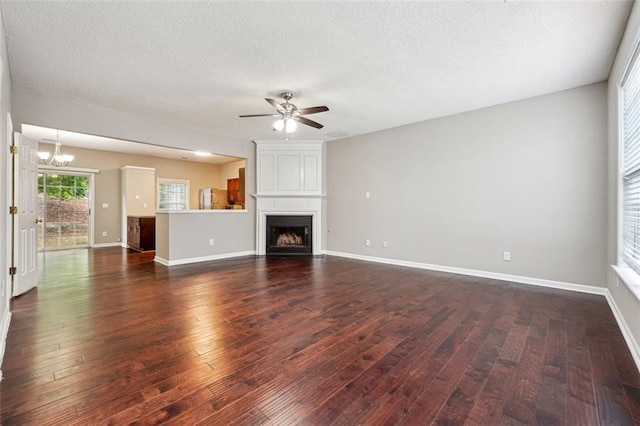 unfurnished living room with a ceiling fan, a chandelier, dark wood-style floors, a fireplace, and a textured ceiling