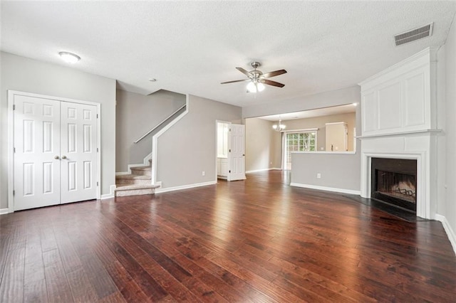 unfurnished living room featuring ceiling fan, dark wood finished floors, stairway, a fireplace, and a textured ceiling