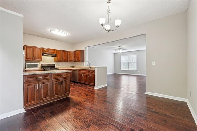 kitchen with appliances with stainless steel finishes, light countertops, under cabinet range hood, a peninsula, and dark wood finished floors