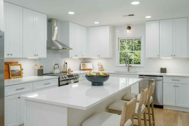 kitchen with visible vents, appliances with stainless steel finishes, a kitchen breakfast bar, wall chimney exhaust hood, and a sink