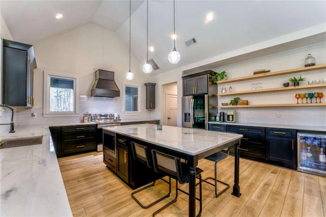 kitchen with stainless steel appliances, tasteful backsplash, wine cooler, light stone counters, and premium range hood