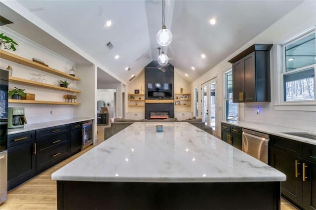 kitchen with tasteful backsplash, stainless steel dishwasher, a kitchen island, and light stone counters