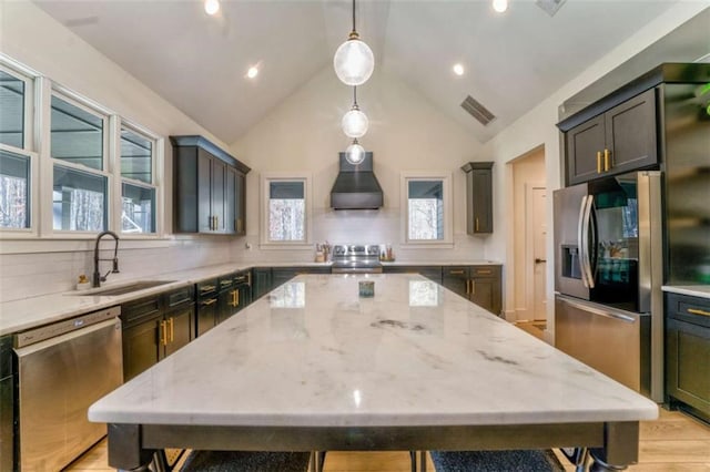 kitchen with appliances with stainless steel finishes, backsplash, sink, hanging light fixtures, and range hood