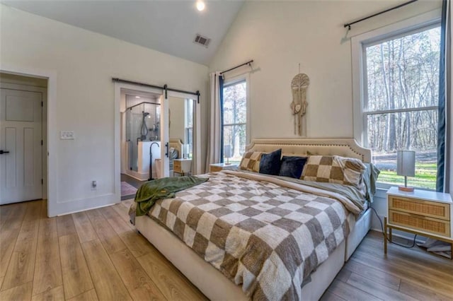 bedroom with a barn door, light hardwood / wood-style floors, multiple windows, and lofted ceiling