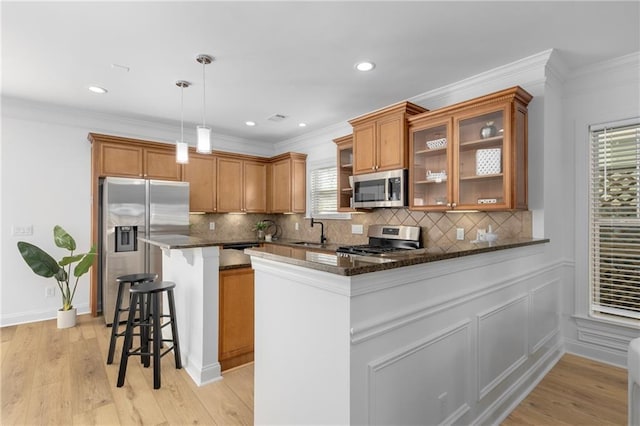 kitchen with kitchen peninsula, appliances with stainless steel finishes, dark stone counters, sink, and pendant lighting