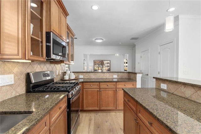 kitchen with stainless steel appliances, light hardwood / wood-style flooring, dark stone countertops, crown molding, and pendant lighting