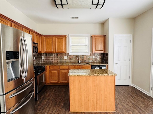 kitchen featuring appliances with stainless steel finishes, dark hardwood / wood-style flooring, light stone counters, sink, and a center island