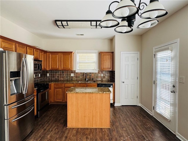 kitchen featuring appliances with stainless steel finishes, light stone counters, sink, a notable chandelier, and a center island