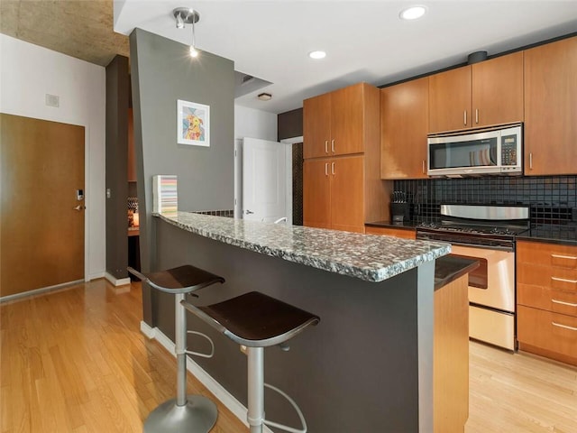 kitchen featuring tasteful backsplash, appliances with stainless steel finishes, a kitchen breakfast bar, and light hardwood / wood-style flooring