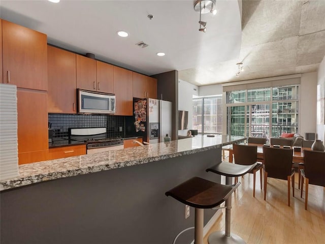 kitchen featuring stainless steel appliances, light stone countertops, backsplash, and light hardwood / wood-style flooring