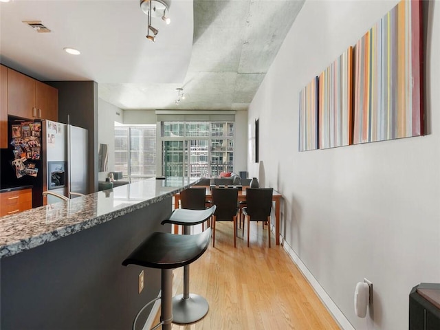 kitchen featuring a breakfast bar area, dark stone countertops, light hardwood / wood-style floors, and stainless steel fridge with ice dispenser