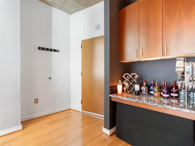 bar with light stone counters and light hardwood / wood-style floors