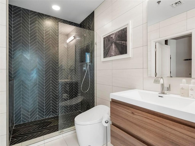 bathroom featuring tile walls, tile patterned flooring, tiled shower, vanity, and toilet