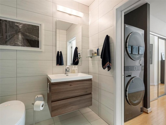 bathroom with vanity, stacked washer and clothes dryer, tile walls, and toilet