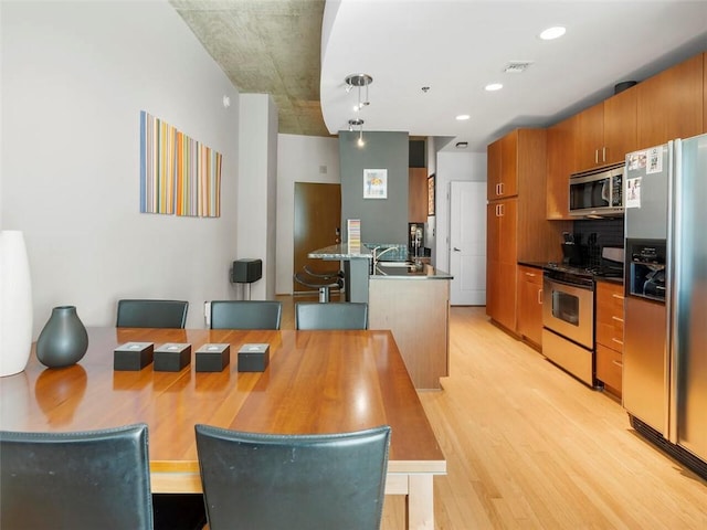 kitchen featuring appliances with stainless steel finishes, sink, light hardwood / wood-style flooring, and decorative light fixtures