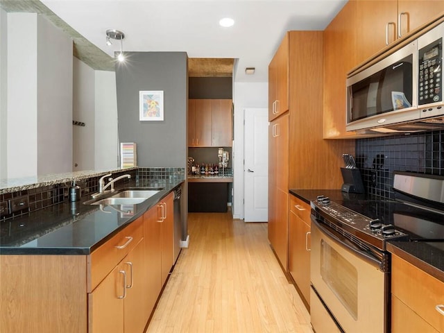 kitchen with sink, light hardwood / wood-style flooring, stainless steel appliances, decorative backsplash, and dark stone counters