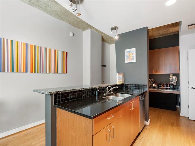 kitchen with sink, dark stone counters, stainless steel dishwasher, kitchen peninsula, and light wood-type flooring