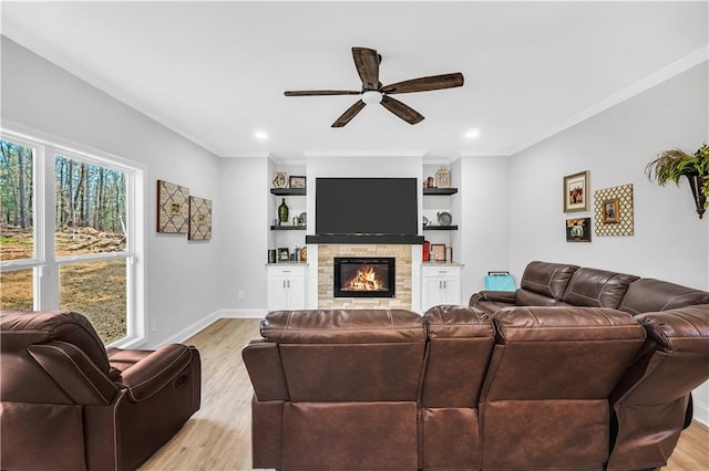 living room with ornamental molding, a stone fireplace, ceiling fan, and light hardwood / wood-style flooring